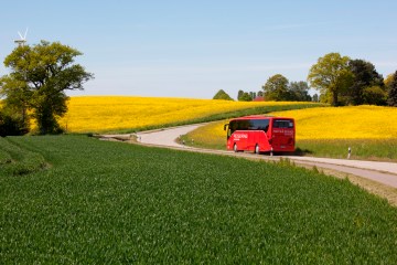 Ein Bus auf einer Landstraße umgeben von grünen und gelben Feldern