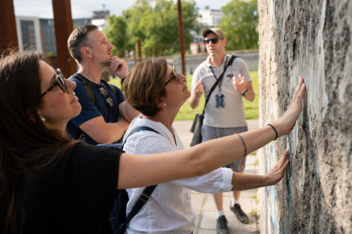 People touch and observe a graffiti-covered wall outdoors.