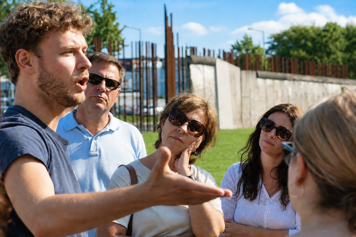 Group listening to a man speak outdoors on a sunny day.