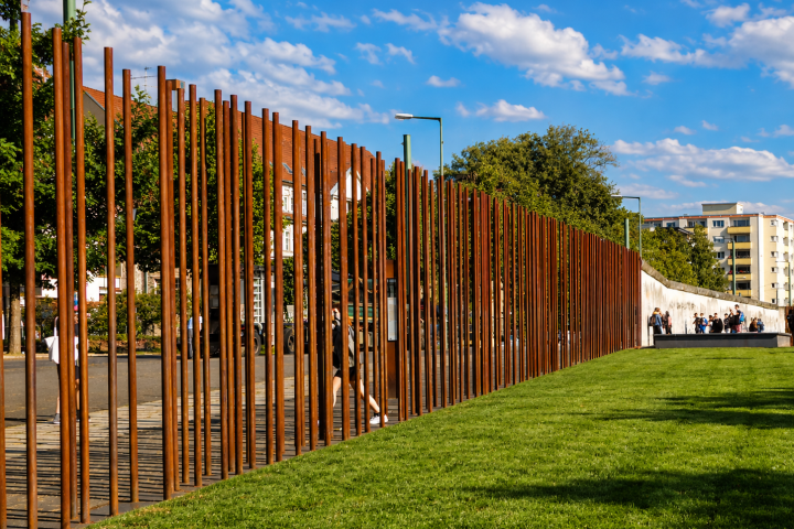 Metal rod sculpture on grassy area with trees and buildings in the background.