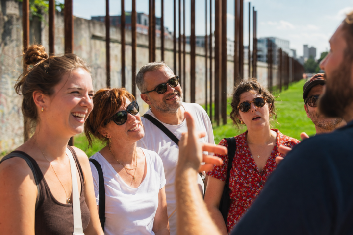 Group of people listening to a guide outside near a wall on a sunny day.