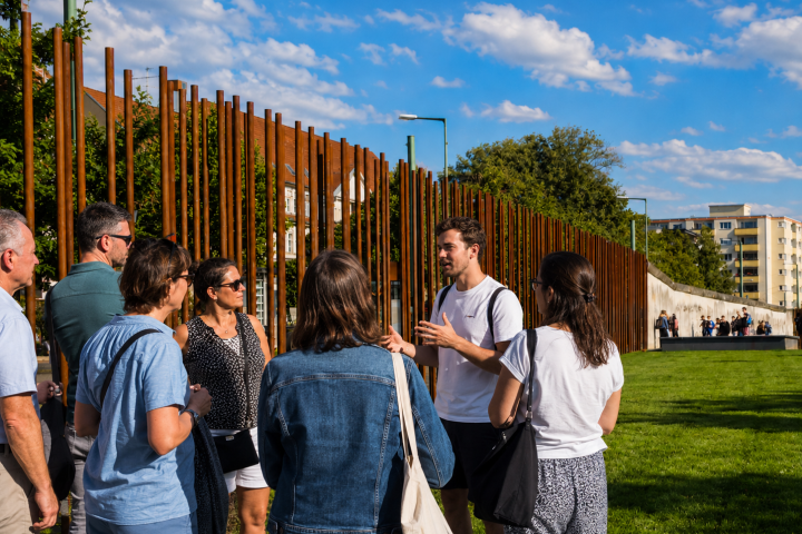 Guide talks to a group of tourists outside near a steel rod art installation.