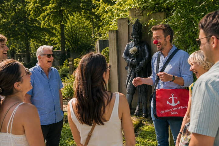 Group of people outdoors, one wearing a red clown nose, near a statue.