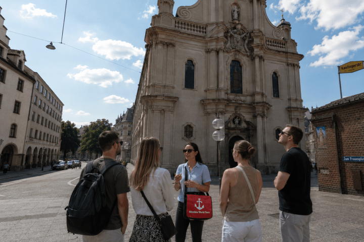 People listening to a guide in front of a historic building on a sunny day.