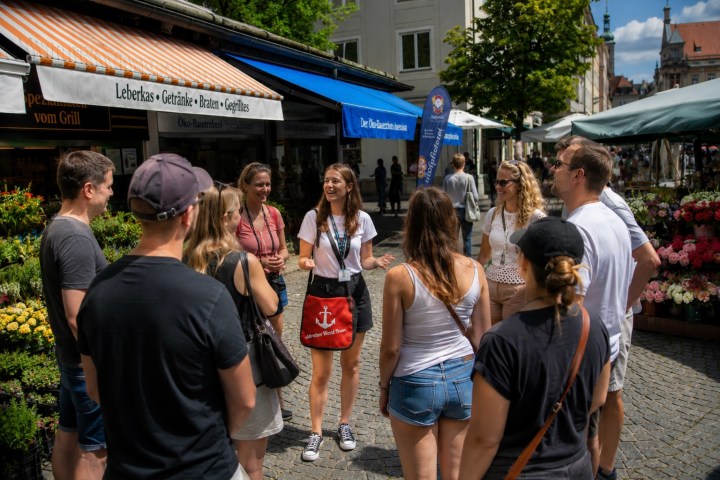 Group of people gathered around a guide in a market area with flower stalls.