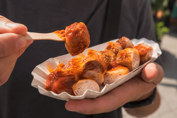 Person holding sliced sausages with sauce in a paper tray.