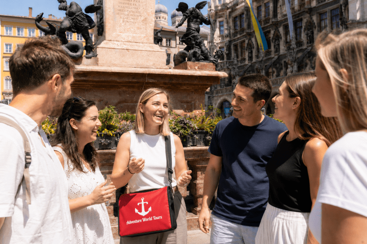 Group of six people chatting near a historic monument in a city square.