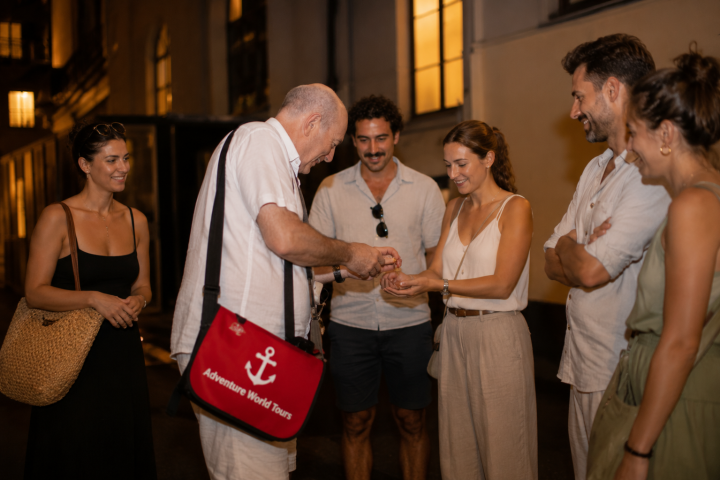 Group of people gathered around a man showing a trick at night.