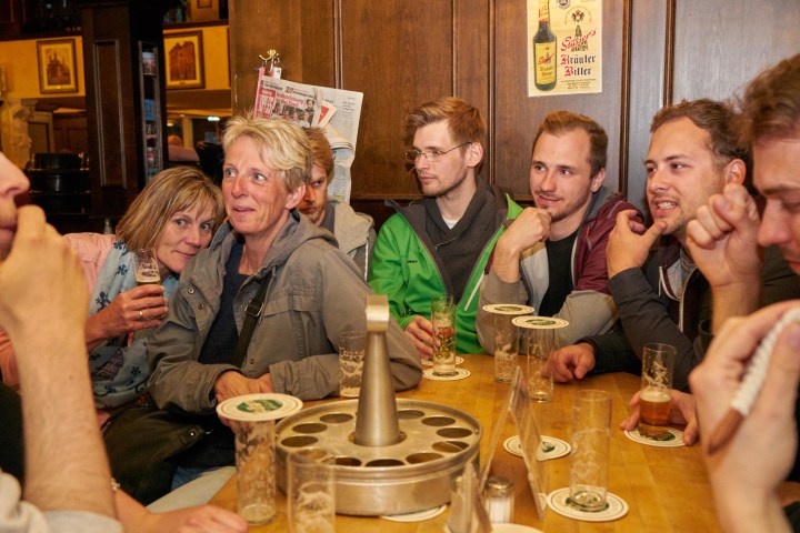 Group of people sitting around a bar table with glasses of beer.