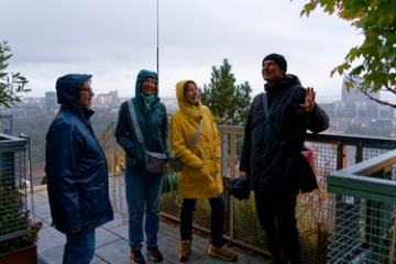 Four people in raincoats standing on a balcony with a city view.