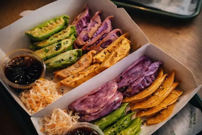 Colorful dumplings and coleslaw with dipping sauce in a tray on a wooden table.