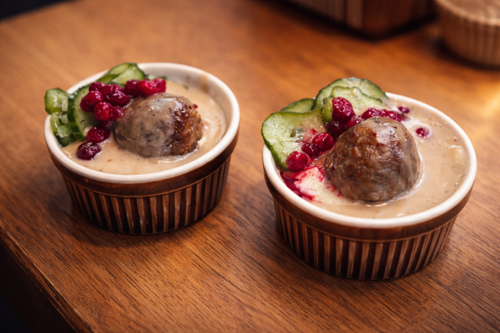 Two bowls with meatball, gravy, cucumber, and berries on wooden table.