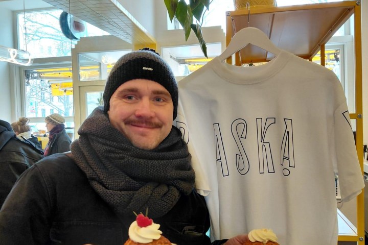 Person in cozy attire holding two pastries with cream and berries, near a white shirt and hanging plant.