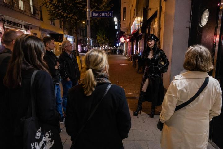 Guide in leather outfit leads a nighttime walking tour on an urban street.