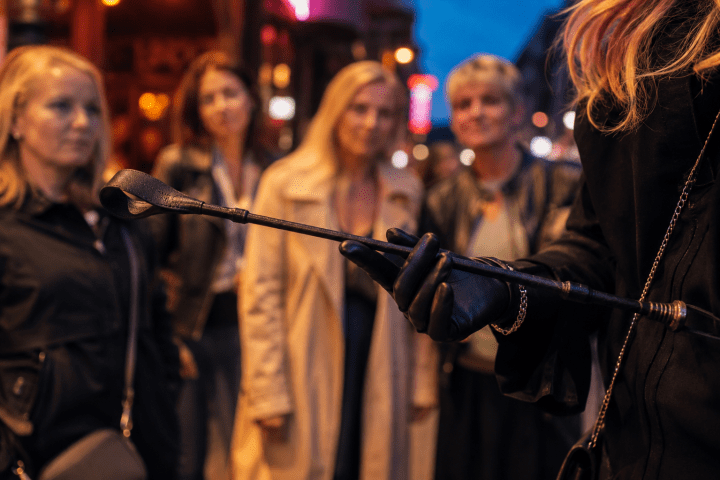 Person holding a whip, four others in background on a city street at dusk.