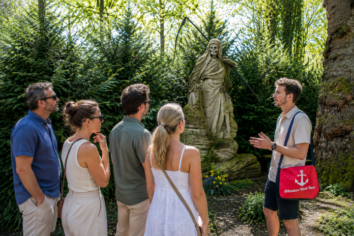 Group of people listening to a guide near a stone statue in a garden.
