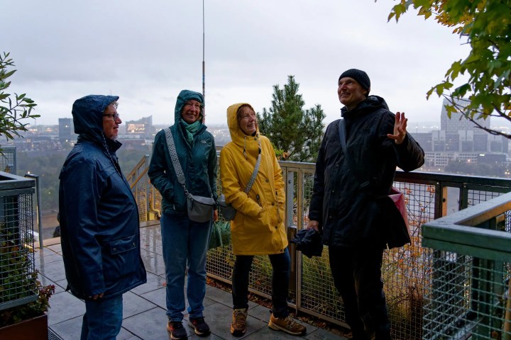 Four people in raincoats smiling on a balcony overlooking a city skyline.