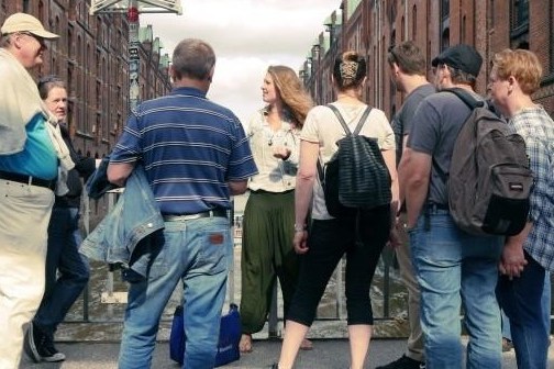 Group of people standing on a bridge between brick buildings.